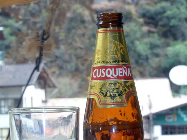 On table there is a bottle and glass with wine. Far there are trees and buildings.