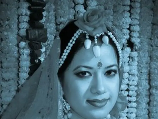 In this image there is a woman smiling, and in the background there are flower garlands.